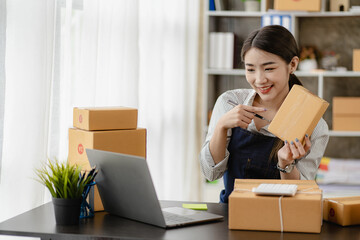 Fototapeta na wymiar beautiful asian woman working at home selling online with yellow box and laptop on taking name orders from customers sme business concept parcel delivery