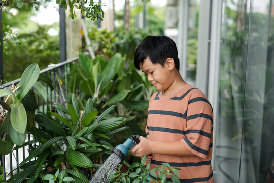 Active school boy watering plants with water can at home on balcony
