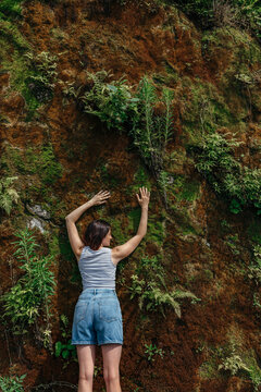 A slender girl clung to a green rock with plants and moss for cooling