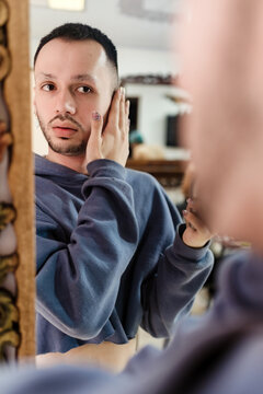 Young gay guy caresses his face in front of the mirror