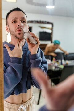 Non binary man shaving his beard