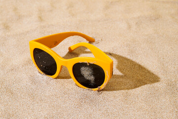 Fototapeta premium yellow sunglasses on the sand of a beach