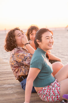 Gen Z friends laughing while sitting at the beach at sunset