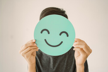 Happy mixed Asian teen boy holding smile emoji face, positive mental health concept