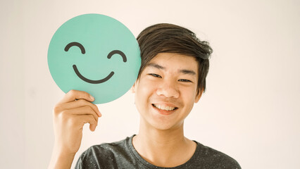 Happy mixed Asian teen boy holding smile emoji face, positive mental health concept