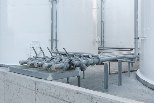 Metal pipes and valves connected to the white storage tank.