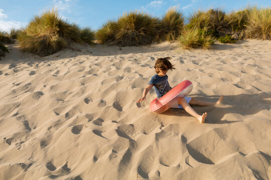 Boy rolling down a dune with a float