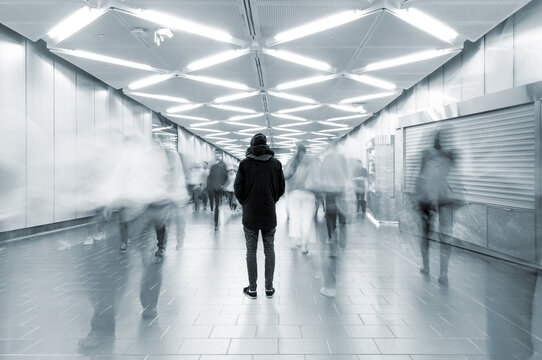 Man from behind standing at busy walkway with people in motion blur