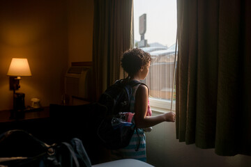 Girl with backpack looks out hotel window