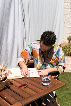 Man drawing in a sketchbook sitting on table outdoors.