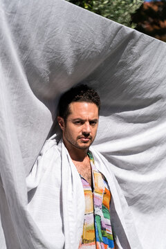 Man looking at camera while standing under hanging fabric.