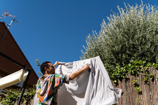 Man Hanging Freshly Washed Clean Sheet Outdoors.