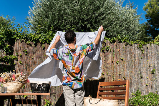 Man hanging freshly washed clean sheet outdoors.