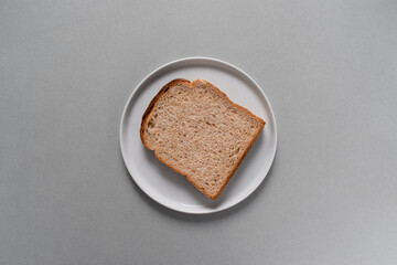 A slice of whole wheat bread on white plate. Gray color background.