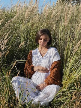 Pregnant woman sitting in hight grass.