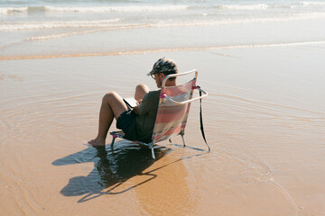 Man on folding beach chair reading at the beach