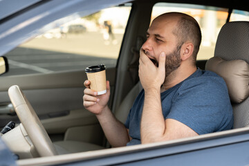 Adult handsome man feeling tired and yawning while driving a car. Driver having coffee early...