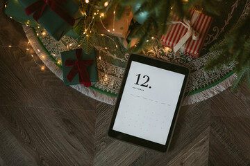 Top view of digital tablet with December calendar on screen laying with presents under Christmas...