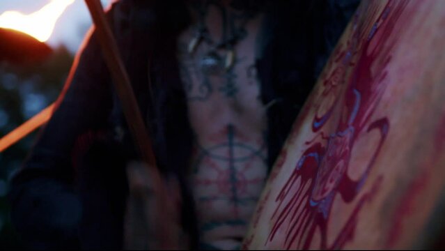 Close-up of a tattooed Viking drumming before the war at dusk in slow motion. Lighted torch