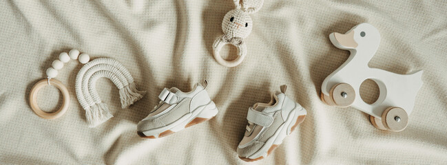 Set of newborn stuff and baby accessories. Cute shoes, wood toys on beige background. Baby shower, infant care concept. Gender neutral parenting. Top view, flat lay, copy space