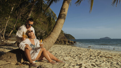 Sexy loving couple in white dress and sunglasses, near palm tree, relax and drinking cocktail Pina Colada. Concept sea beach resting tropical tourism summer holidays wedding love family vacations