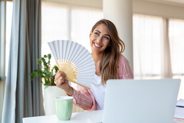 Tired overheated young woman hold wave fan suffer from heat sweating indoor work on laptop at home...