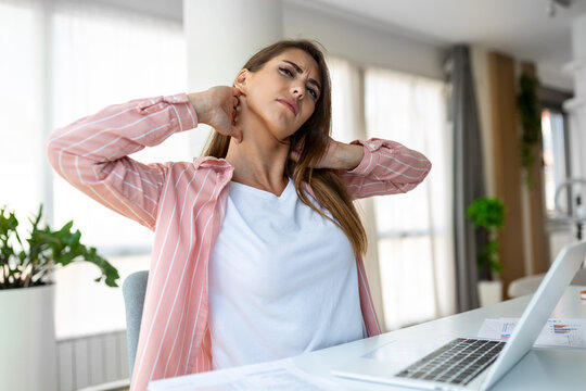 Feeling exhausted. Frustrated woman looking exhausted and massaging her neck while sitting at her working place