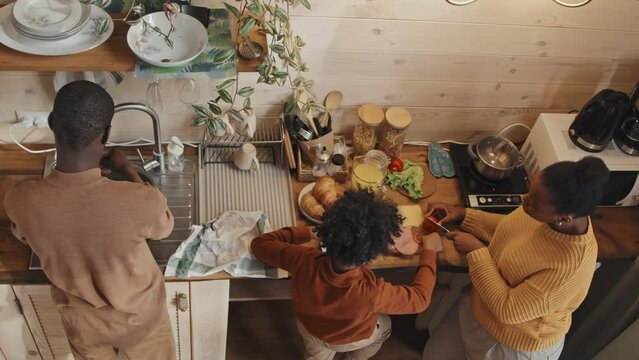 From above view of modern African American family of three standing in country house kitchen cooking meal together