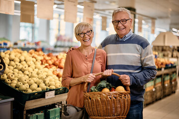 Happy senior couple shopping groceries in supermarket and looking at camera.