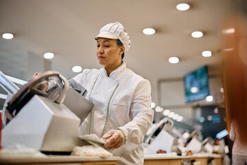 Supermarket clerk using slicer while working at delicatessen section.
