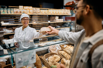 Happy supermarket baker serving male customer. - obrazy, fototapety, plakaty