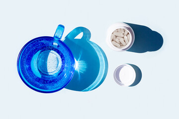 Pills and glass of water on blue background. Medicine, healthcare concept