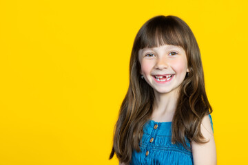 A cute little schoolgirl girl smiles broadly, her front milk teeth fell out in her mouth. The concept of a pediatric dentist and tooth loss. Empty space for signature.