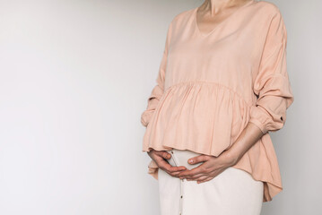 Pregnant woman in pink dress touching belly, preparing go to maternity hospital for childbirth. Pregnancy, maternity, preparation, baby expectation concept. 40 weeks of pregnancy. White background