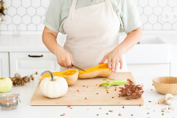 Woman hands cutting a butternut pumpkin in modern white kitchen. Homemade autumn pumpkin soup recipe. Cooking at home 