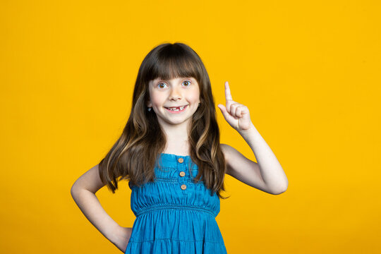 Cute little smiling girl raised her index finger up. An idea has come or points to a place for an inscription for a promotion or discount. Isolated on a yellow background.