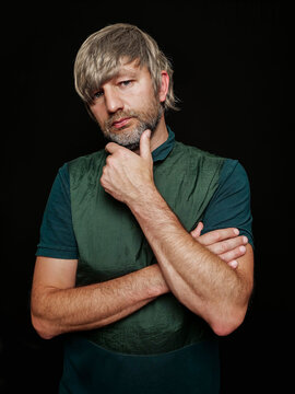Portrait of a man in his 40s with grey beard and hair on dark background. Hands crossed. Slim body type. Friendly face. Studio image of a male model.