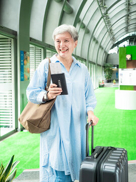 Portrait of senior adult elderly asian woman 60s smiling standing with suitcase luggage bag and holding passport with ticket for travel concept.
