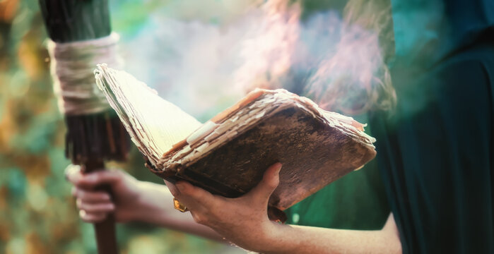 Young witch with spell book in green forest, closeup