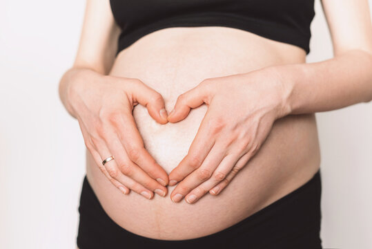 Woman hands making heart on pregnant belly. Pregnancy, maternity, preparation, baby expectation concept