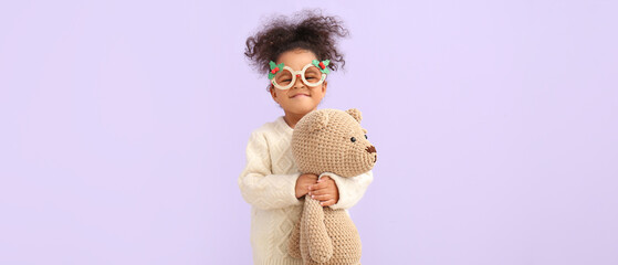 Cute African-American baby girl with toy bear on lilac background