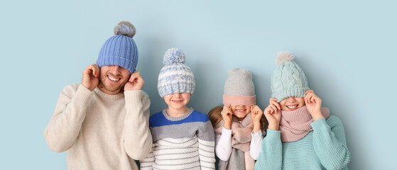Funny family in winter clothes on light blue background