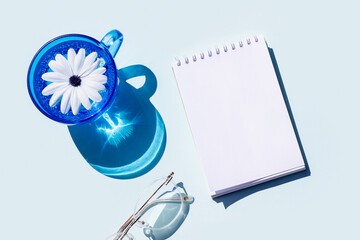 Empty notepad, glass of water and eyeglasses with strong shadows on blue background. Creative mockup. Top view, flat lay, Still life
