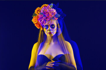 Young woman with painted skull on her face for Mexico's Day of the Dead (El Dia de Muertos) against blue background