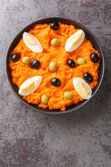 Omek Houria is a Tunisian salad, made with carrots, harissa, garlic, vinegar, olive oil served with egg and olives closeup in the plate on the table. Vertical top view from above