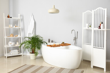 Interior of modern bathroom with folding screen, shelving unit and houseplant