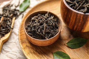 Bowl with dry tea leaves on wooden background