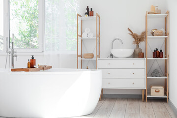 Stylish interior of bathroom with modern bathtub and shelf units with bath accessories