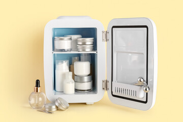 Small refrigerator with cosmetic products on color background