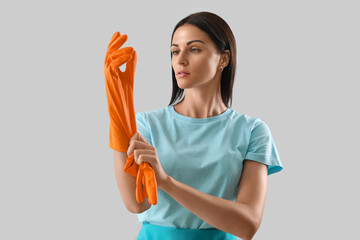 Beautiful woman putting rubber glove on light background